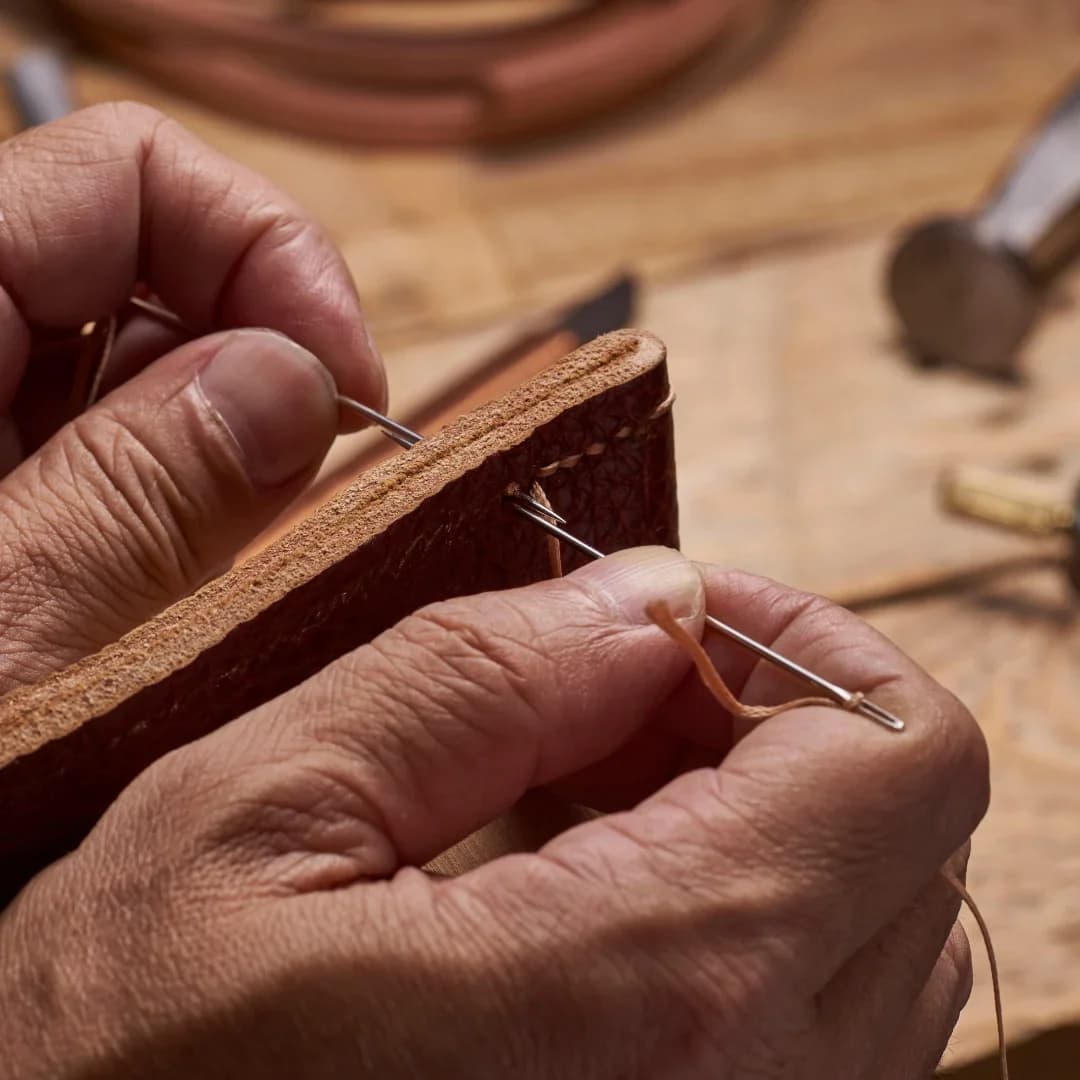 Hands saddle stitching a piece of brown leather