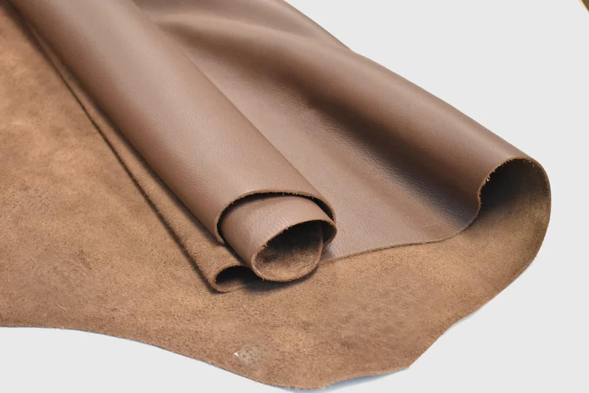 Rolled medium-brown leather hide showing its smooth grain and suede underside