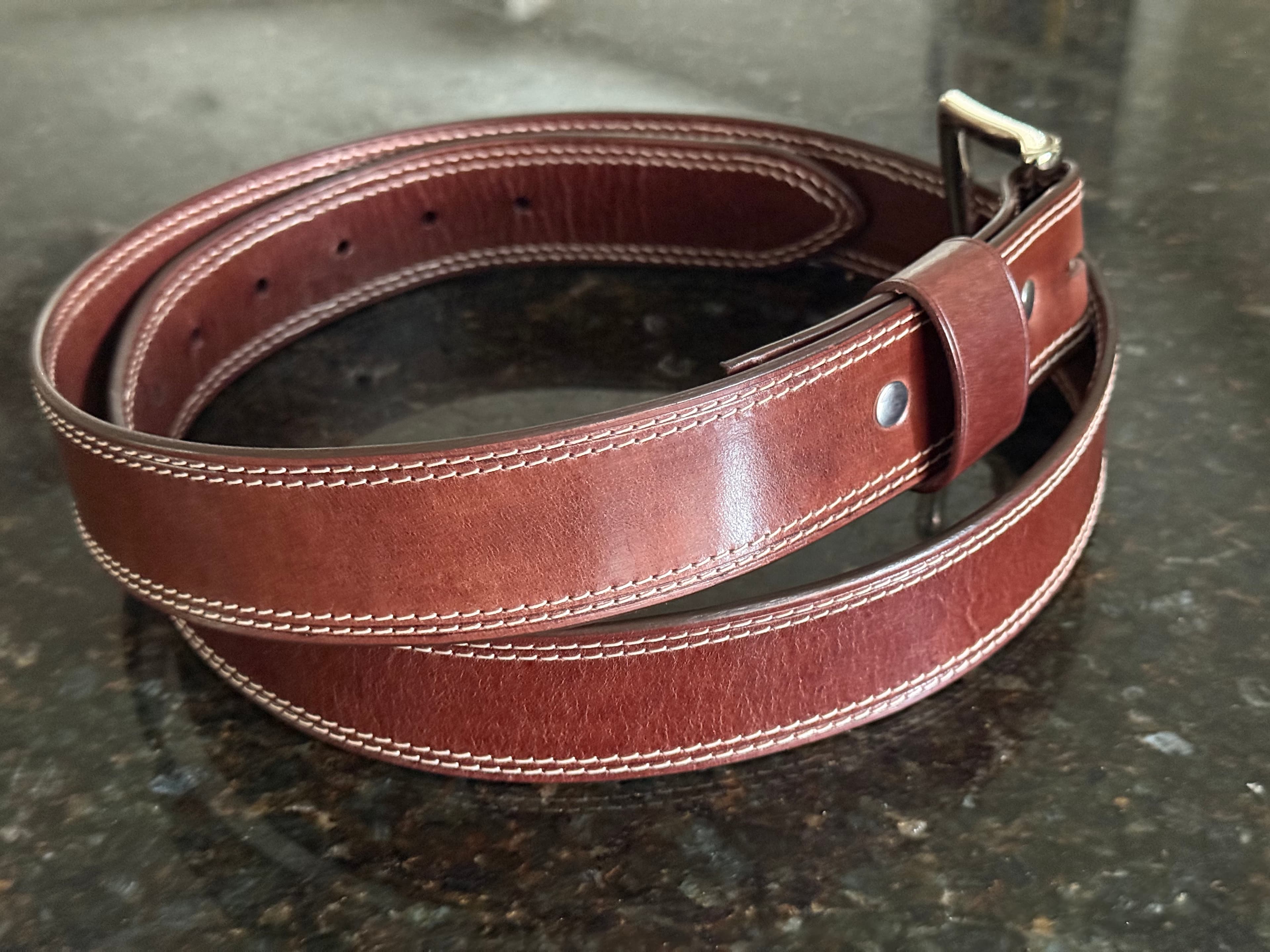 The polished Maya belt coiled on a dark granite kitchen counter, with rich reddish tones and an even sheen.