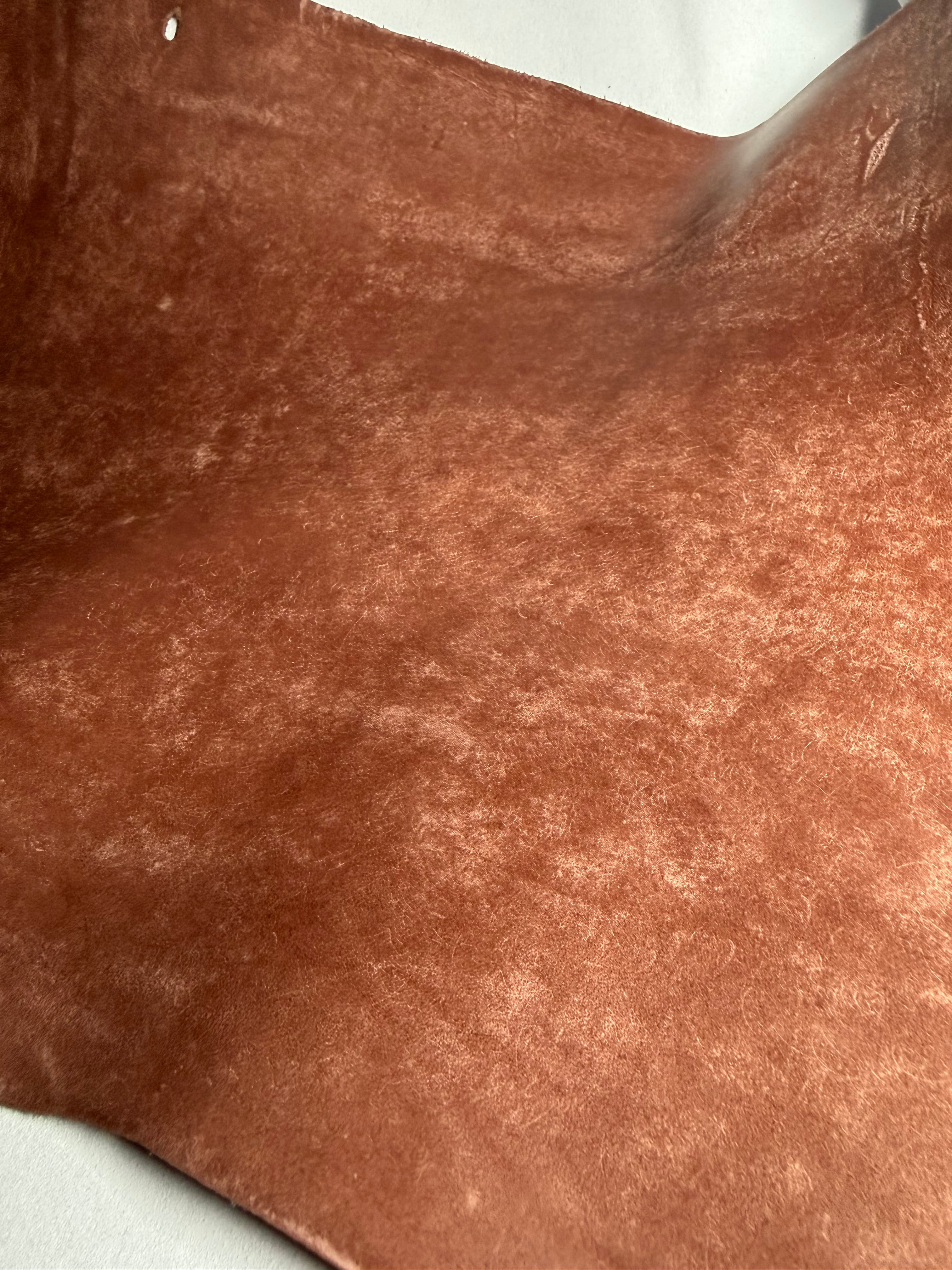 Maya leather on a white leather background, with pale mottled marks scattered across a reddish-brown surface.