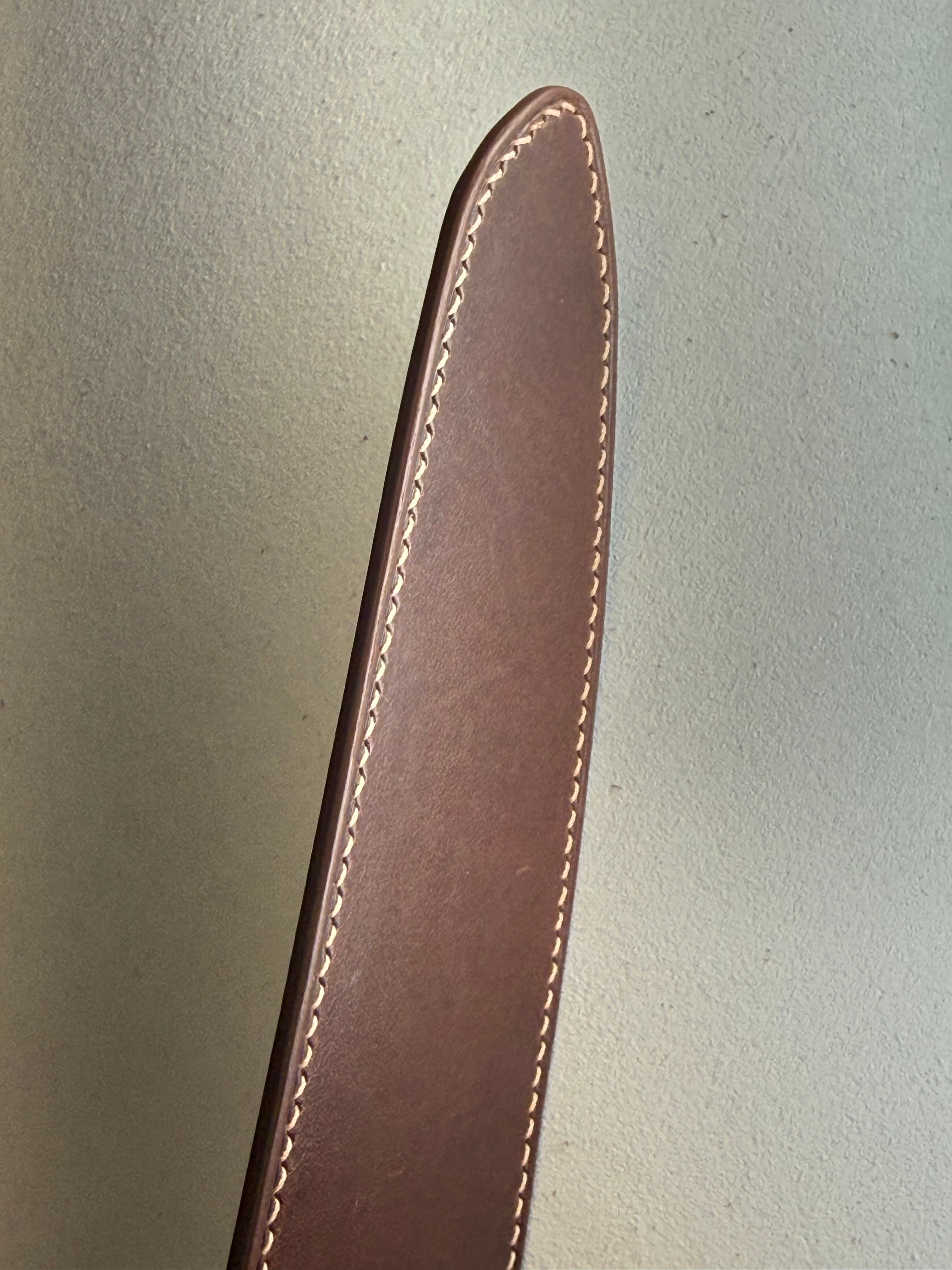 The tapered tip of a Maya kitchen-knife sheath with a single row of pale hand stitching and a medium-brown painted edge.