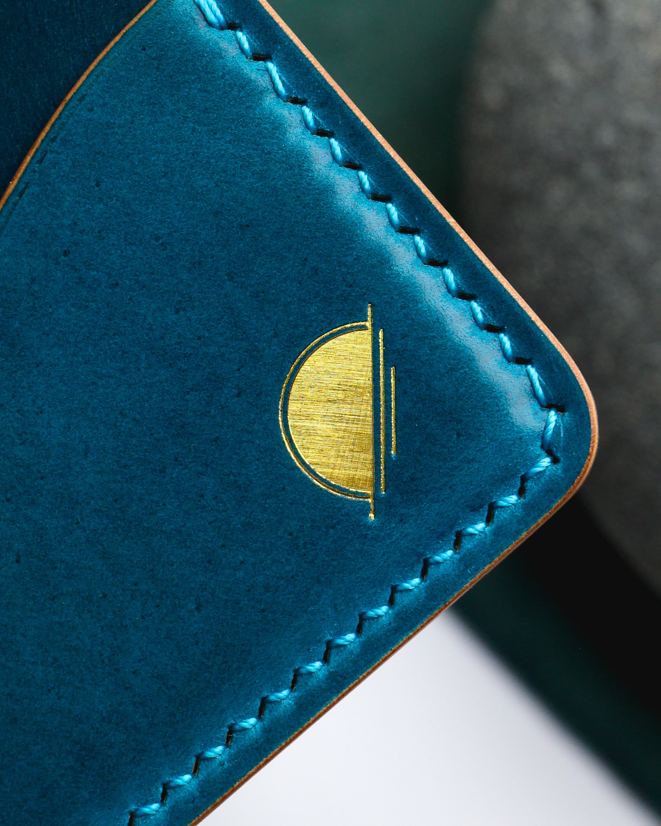 Close detail of a blue leather wallet with contrasting blue stitching and a gold maker's mark.